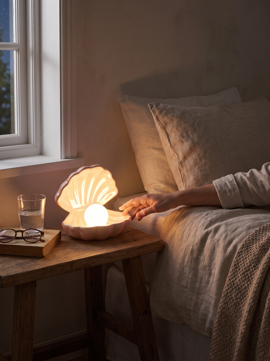 A small ceramic shell night light glowing softly on a bedside shelf